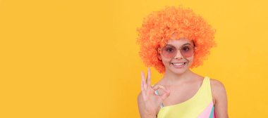 happy teen girl in sunglasses on yellow background presenting product with ok, copy space, advert. Funny teenager child on party, poster banner header with copy space