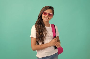 Bilgi günü. Eğitim konsepti. Mavi arka planda güneş gözlüklü çocuk. 1 Eylül. Mutlu çocukluk. Okul çantalı çocuk. Neşeli genç kız sırt çantası taşıyor. Okula geri dön..