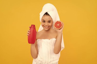 Sarı arka planda greyfurt şampuanı şişesiyle havlu neşeli kız..
