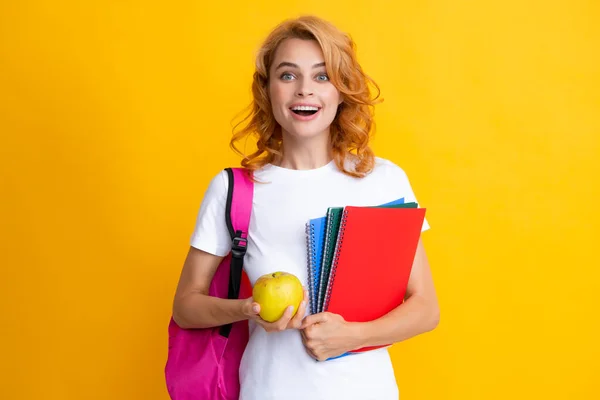 Excited redhead young woman student with backpack hold notebooks, isolated on yellow background studio Education in high school university college