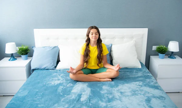 Morning Meditation on bed. Teenager child practicing meditation at bedroom. Relaxed girl on bed in lotus pose and meditating, morning yoga in bedroom