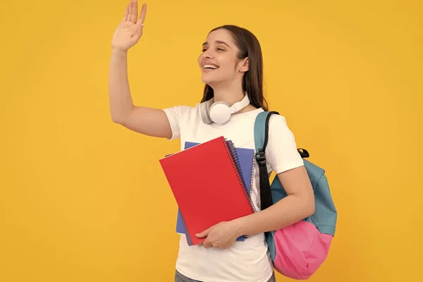 back to school. modern education concept. happy student hold notebook waving hello. girl holding notebook on yellow background. private teacher with copybooks and headphones.