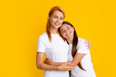 Mother and daughter teenager girl in t-shirt embrace cudding isolated on yellow color background studio. Mothers day love family