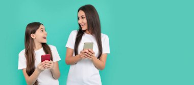 Anne ve kız çocuk afişi, kopyalama alanı, izole edilmiş arka plan. Şaşırmış anne ve kızı mavi arka planda akıllı telefondan sohbet ediyorlar.