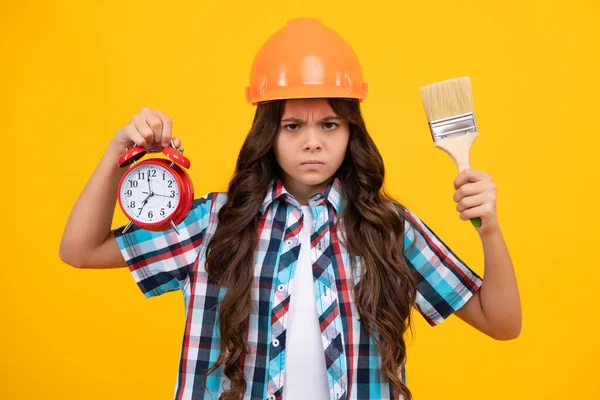 Serious angry teenager child painter in helmet with painting brush. Child in hard hat and alarm. Kid builder painter on construction site. Time to renovation and repair