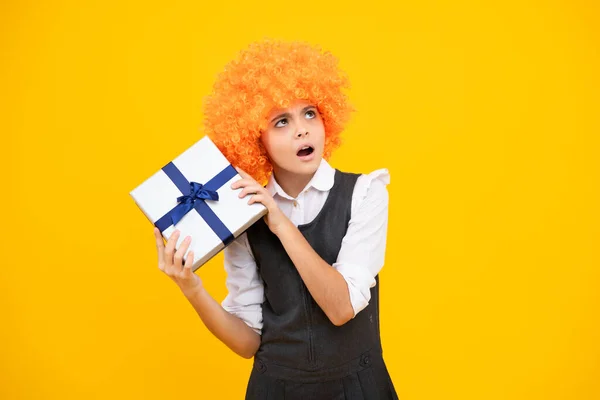 Child with gift present box on isolated yellow background. Presents for birthday, Valentines day, New Year or Christmas. Surprised face, surprise emotions of teenager girl