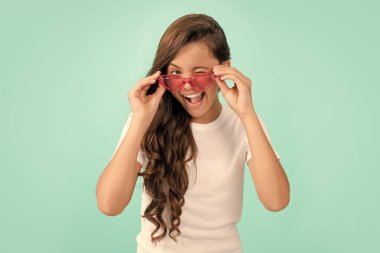 Kırmızı gözlüklü komik çocuk. Eğlenceli genç kız eğleniyor. Güneş gözlüklü neşeli çocuğun kıvırcık saçları var. Moda aksesuarı. Sıradan bir yaz stili. çocukluk mutluluğu. Şık parti görünüşü.