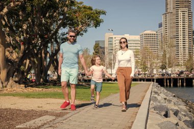 Baba, anne ve çocuk parkta. Arkadaş canlısı aile yazın eğleniyor. Küçük çocuklu genç ebeveynler. Anne, baba ve oğul birlikte rahatlayın. Evlat edinme ve sadaka. Aile günü. dostluk.