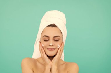 Genç kız mavi arka plana yüz kremi sür..