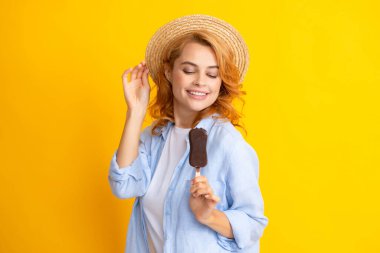 Portakal sarısı arka planda dondurma yiyen güzel bir kadının portresi. Çikolatalı dondurma yiyen yaz şapkalı bir kız. Mutlu heyecanlı yüz ifadesi kadın portresi