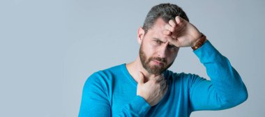 mature man with beard has heacache suffer from headahce on grey background, malaise. Man face portrait, banner with copy space