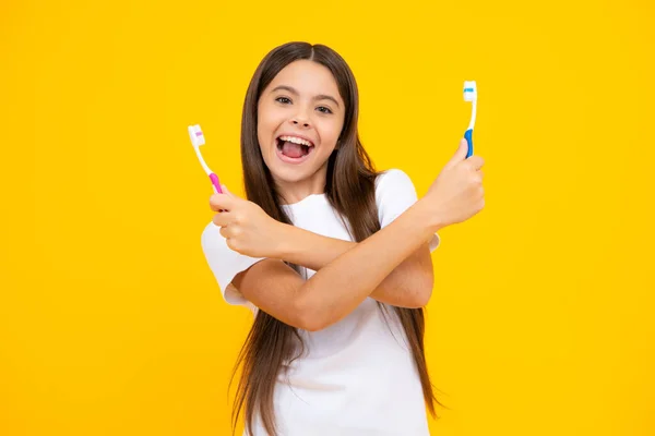 Portrait of caucasian teen girl holds a toothbrush brushing her teeth, morning routine, dental hygiene, isolated on yellow background. Excited teenager, glad amazed and overjoyed emotions