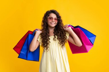 Beautiful fashion teenager child girl with shopping bags on yellow background. Shopaholic shopping and fashion. Kid with shopping sale bags. Happy teenager, positive and smiling emotions