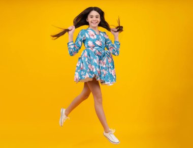 Mutluluk, özgürlük, hareket ve çocuk. Genç kız sarı arka plandan atlıyor, komik bir atlayış.