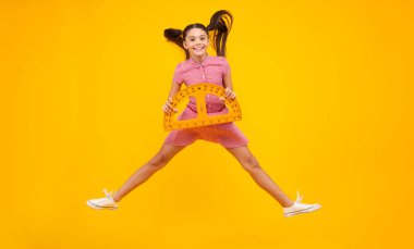 Okul kızı geometri dersi için ölçü tutuyor, sarı arka planda izole edilmiş. Ölçüm aletleri. Öğrenci matematiği okuyor. Mutlu ergen, pozitif ve gülümseyen liseli kız duyguları