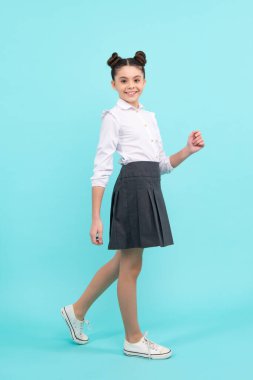 Tişörtlü, etekli, sevimli, sevimli, neşeli, neşeli, genç bir kız çocuğu, parlak mavi arka planda izole edilmiş. Mutlu ergen, pozitif ve gülümseyen gençlik duyguları