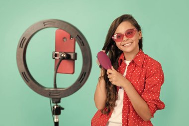 happy teen girl combing long hair with hair brush in sunglasses talking on selfie led smartphone beauty blog blogging online, hair loss.