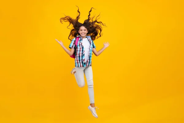 Schoolgirl in school uniform with backpack. Teenage girl student on yellow isolated background. School leisure. Crazy run and jump. Learning and education children