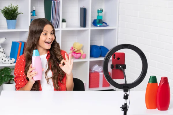 Child vlogger hold hair conditioner or shampoo bottle making video blog on phone. Blogging weblog and vlog. Teen girl blogger influencer recording video for social media