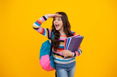 Amazed teenager. Schoolchild, teenage student girl hold book on yellow isolated studio background. School and education concept. Back to school. Excited teen girl