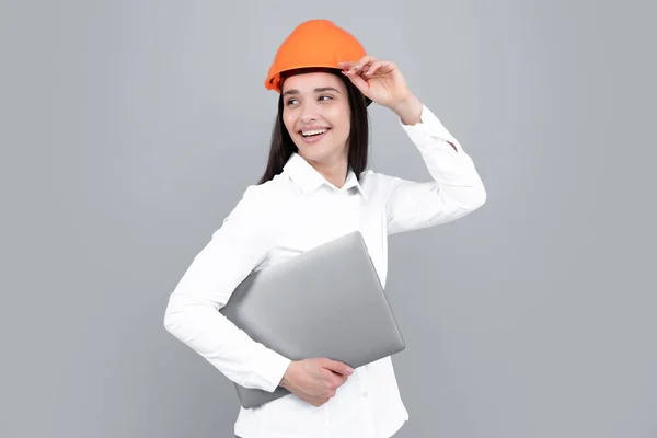 Young beautiful architect woman in hard hat helmet hold laptop computer over gray background. Female builder in helmet for advertising sign