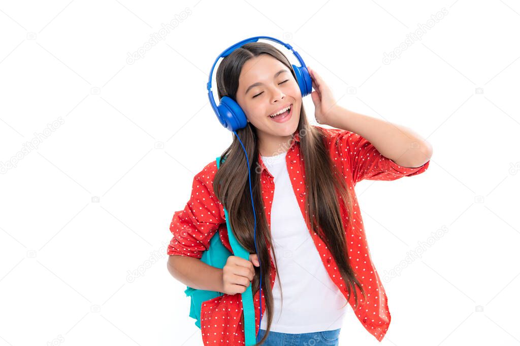 Amazed child singing. Back to school. Schoolgirl student in headphones with school bag backpack on isolated studio background. School and education concept. Teenager girl in school uniform