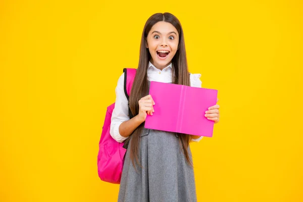 Excited face. Schoolgirl, teenage student girl hold book on yellow isolated studio background. School and education concept. Back to school. Amazed expression, cheerful and glad
