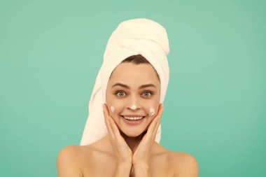 Mutlu genç kız mavi arka plana yüz kremi sürüyor..