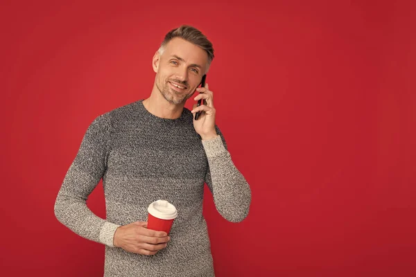 cheerful handsome man wear sweater hold phone and coffee cup, conversation.
