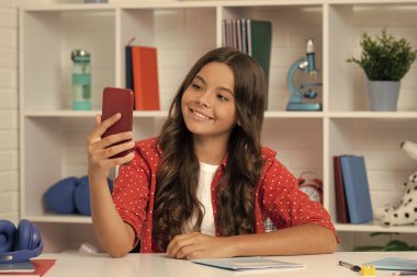 happy kid making selfie in classroom. september 1. child making video blog. blogging on phone. vlogger with cellphone. young influencer. teen girl blogger use smartphone. back to school.