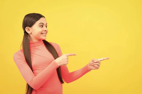 明るい子はコピースペースで指を指してる 黄色の背景に可愛い10代の女の子の広告 幸せな子供の肖像画 発表だ 買い物の販売と割引 提案してくれ 商品提案 — ストック写真
