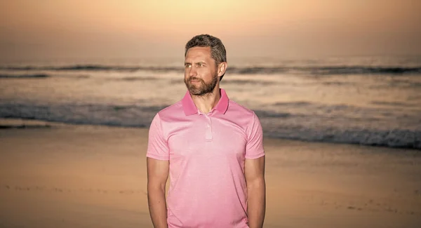 smiling bearded man over the sea on sunset summer beach, summer fashion.