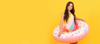 happy kid in swimming suit with doughnut inflatable ring on yellow background. Banner of summer child girl in swimsuit, studio poster header with copy space