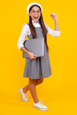 Excited face. Smart little boy with laptop in casual clothes isolated over yellow background. Excited teenager school girl
