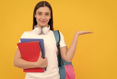 Kulaklıklı neşeli kadın, sarı arka planda ürün sunan defteri tutuyor. Kopya alanı, Eylül.