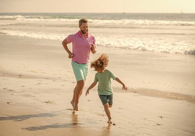father and son running on morning beach. family travel weekend and vacation. fathers or family day. daddy with kid boy on summer day. dad and child having fun outdoors. childhood and parenting.