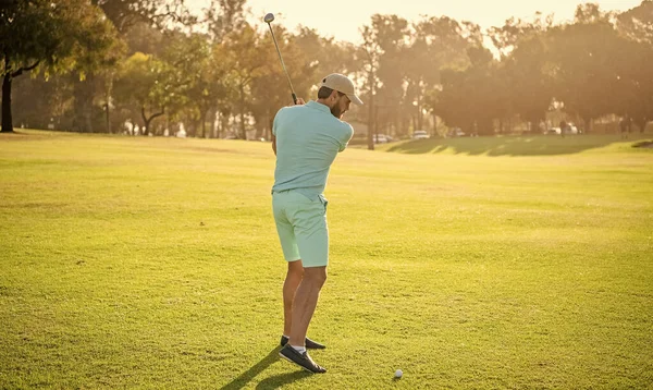 back view of male golf player on professional course with green grass, recreation.