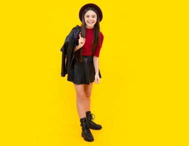 Happy teenager smiling girl. Teenager child girl casual leather skirt posing isolated on yellow background in studio. Kids lifestyle concept
