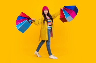 Funny teen girl hold shopping bag enjoying sale isolated on yellow. Portrait of teenager schoolgirl is ready to go shopping. Autumn shopping sale