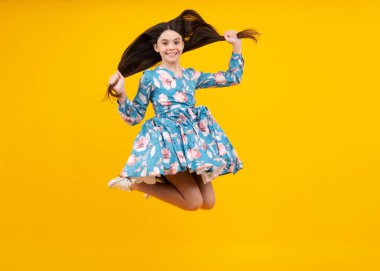 Happiness, freedom, motion and child. Young teenager girl jumping in air over yellow background. Excited face. Amazed expression, cheerful and glad