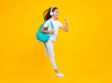 School girl, teenager student in headphones on yellow isolated studio background. School and music education concept. Back to school. Jump and run, jumping child