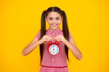 Portrait of teenage girl with clock alrm, time and deadline. Studio shot isolated on yellow background. Happy teenager, positive and smiling emotions of teen girl