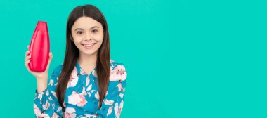 smiling kid with long hair hold shampoo bottle, advertisement. Banner of child girl hair care, studio poster header with copy space