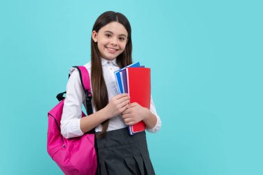 Schoolchild, teenage student girl with school bag backpack hold book on blue isolated studio background. Children school and education concept
