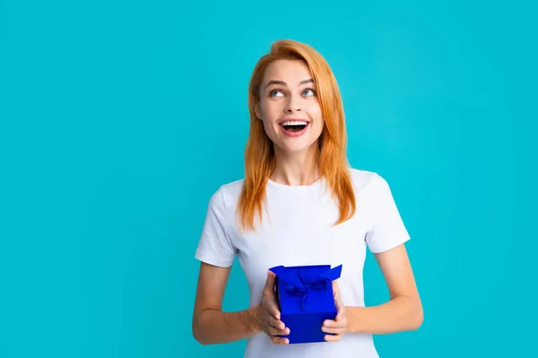 Woman with gift. Portrait of excited young girl holding gift box, isolated blue background. Pretty girl with present