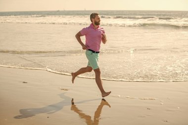 Koşucu özgürlüğü hisseder. Sabahın tadını çıkarıyorum. Dayanıklılık ve dayanıklılık. Olgun sporcu okyanusta kazanmak için hızlı koşar. Sabah sporu aktivitesi. Sahilde koşan sağlıklı bir adam. enerjik yaz.
