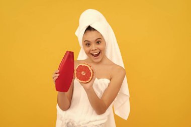 Sarı arka planda greyfurt şampuanı şişesi olan havluyla hayrete düşmüş genç bir çocuk..