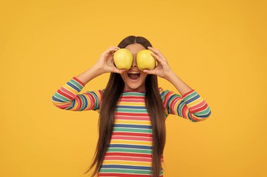 Mutlu kız çocuğu, elmalı meyveyi gözlerinde tutarken iyi eğlenceler sarı arka plan, göz sağlığı.