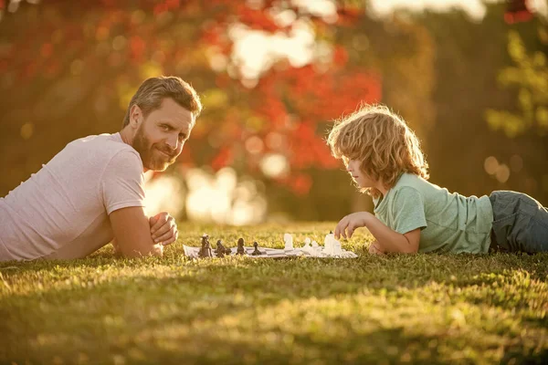 Mutlu bir aile babası ve oğlu parkta yeşil çimlerde satranç oynuyorlar, mantıklı bir spor..