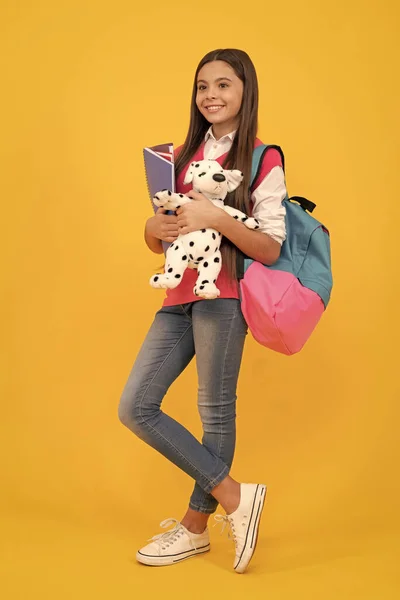 happy teen school girl with backpack and copybook hold toy on yellow background, back to school.